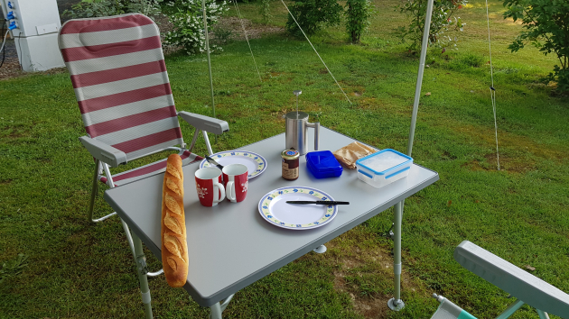 Campingtisch mit Tellern, Kaffeekanne und einem Baguette