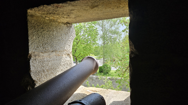 Das Rohr einer Kanone, das durch ein Fenster in einer Mauer schaut